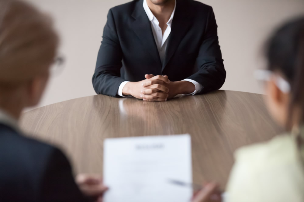 man with hands folded at end of table